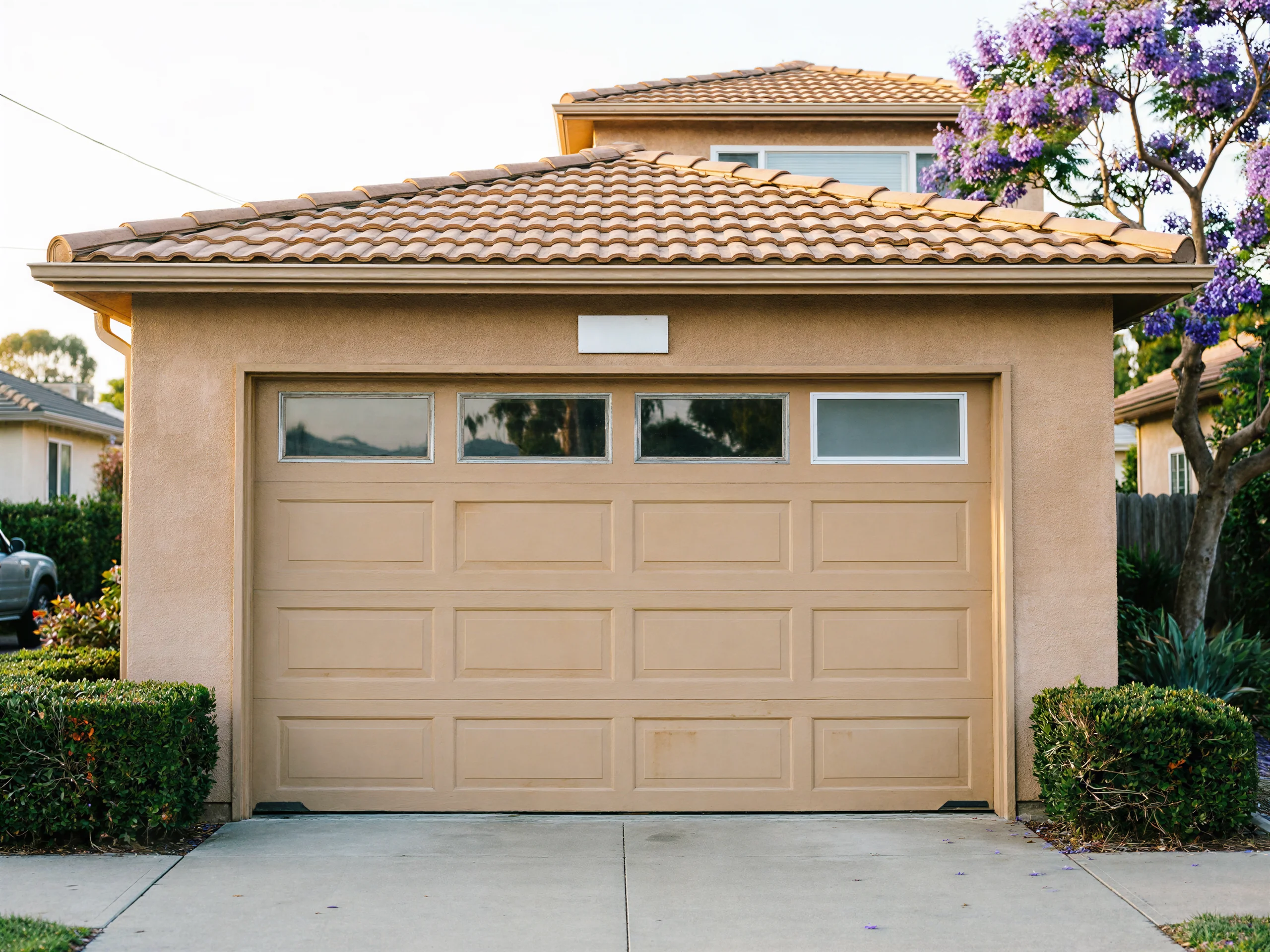 A beige garage door with four windows is on a stucco house.